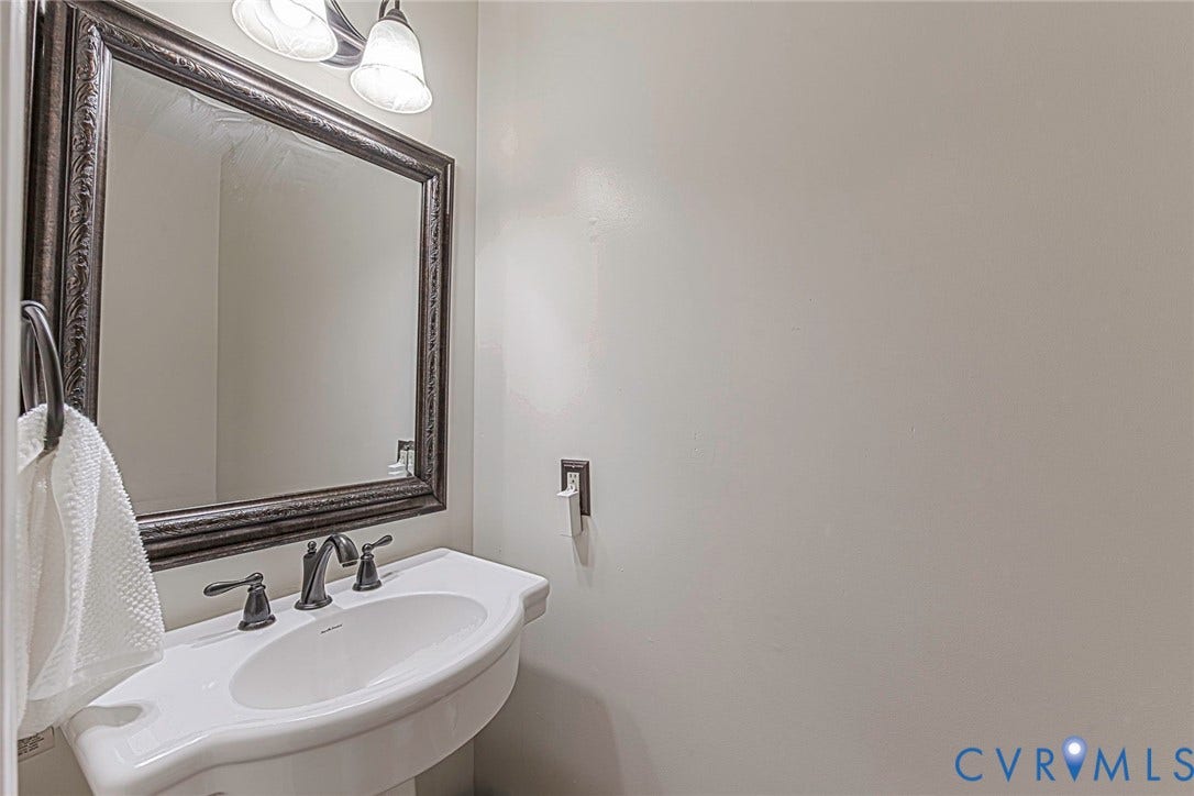Pedestal sink with a dark-toned faucet, framed mirror, and coordinating wall-mounted light fixture