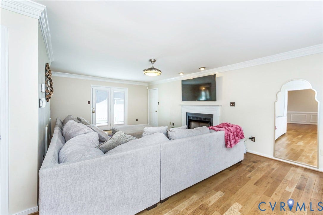 Living area featuring wood-finish flooring, a fireplace with a white mantel, and crown molding