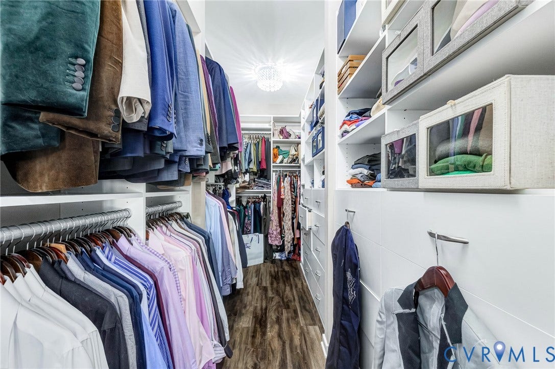 Walk-in closet featuring extensive built-in shelving, multiple hanging rods, integrated drawers, wood-finish flooring, and a central ceiling light fixture