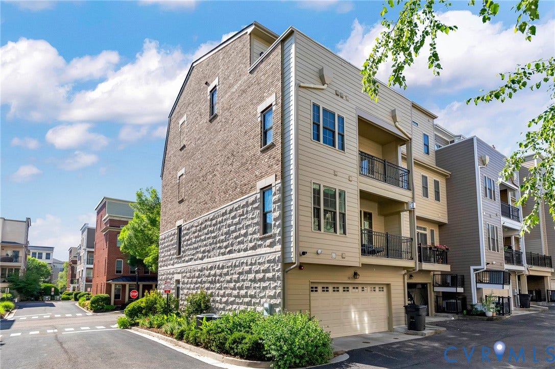 Multi-story townhome featuring a two-car garage, multiple balconies with black metal railings, and a facade combining brick and textured stone