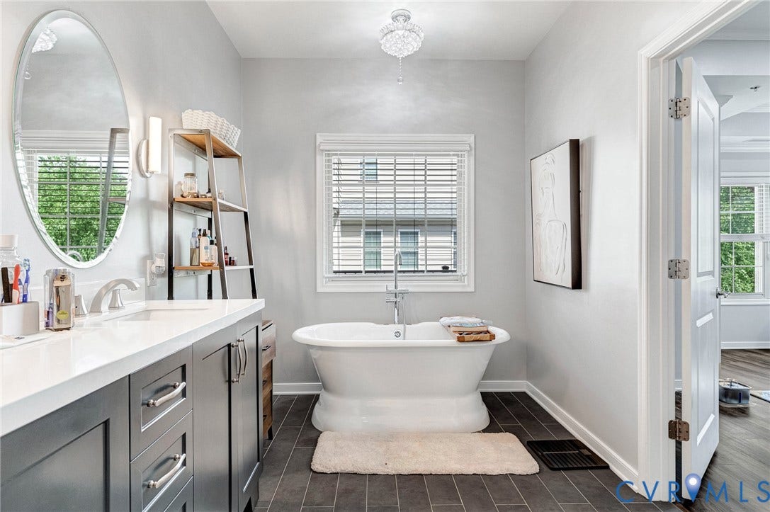 Freestanding soaking tub with a floor-mounted faucet, complemented by a single vanity featuring a white countertop and dark cabinetry
