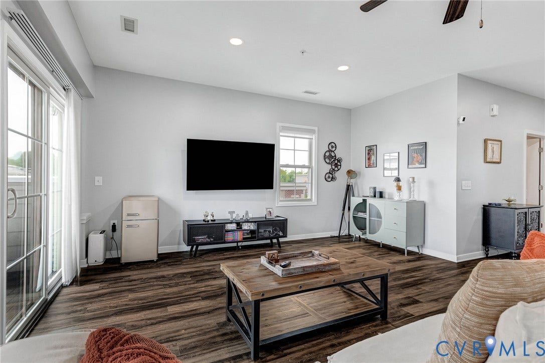 Spacious living area featuring wood-finish flooring, light gray walls, recessed lighting, and a ceiling fan