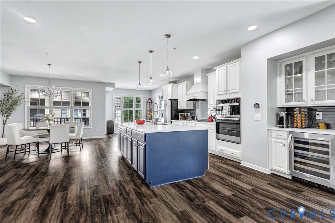 Open-concept kitchen and dining area featuring wood-finish flooring, a blue island with a light-colored countertop, white cabinetry, and recessed lighting