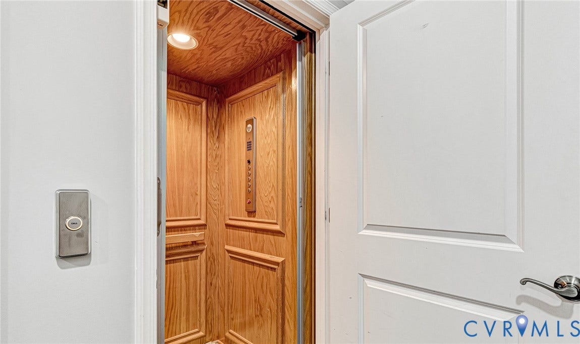 Residential elevator featuring wood-paneled interior walls, recessed lighting, and a brushed metal control panel
