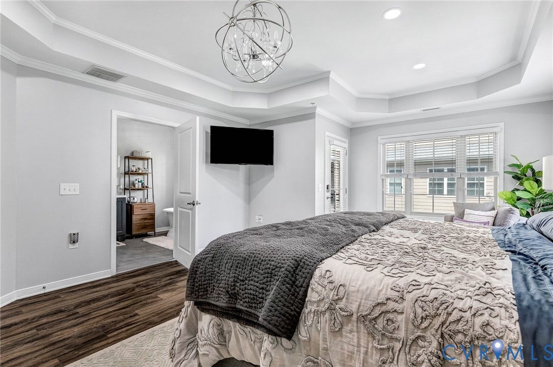 Bedroom featuring wood-finish flooring, a tray ceiling with crown molding, and a contemporary chandelier