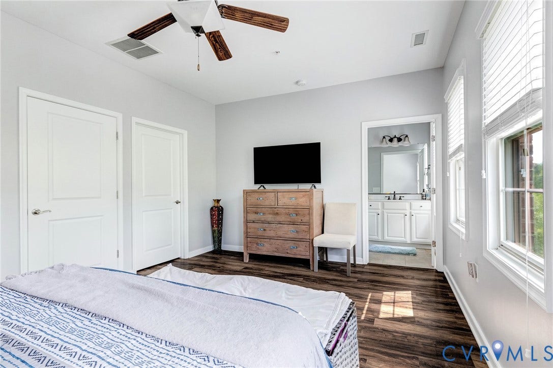 Hardwood-finish flooring throughout, featuring a ceiling fan with wood-finish blades, two panel doors, and multiple windows with blinds