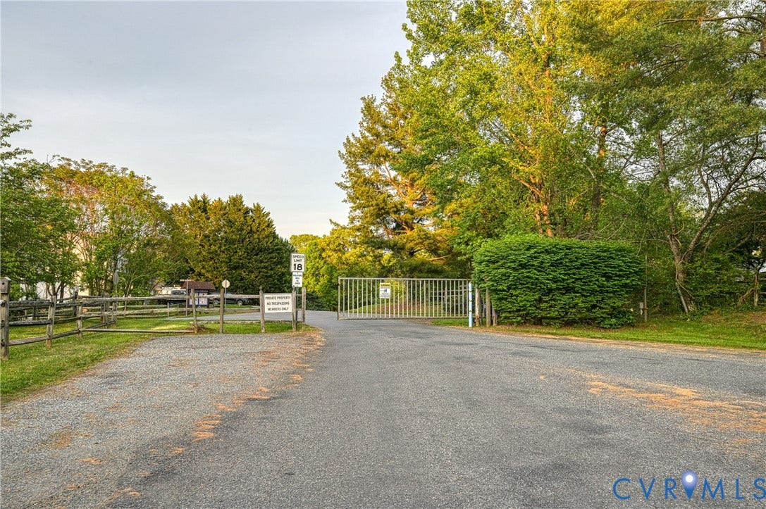 519 N Timber Tribe, Lake Anna, Mineral, VA 23117 Gated entry with a gravel and asphalt driveway, bordered by a split-rail fence and mature trees