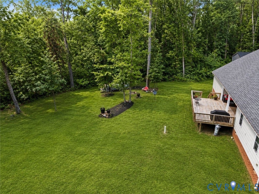 Expansive rear yard featuring a large wooden deck, mature trees, a fire pit area with stone surround, and an adjacent wooded perimeter