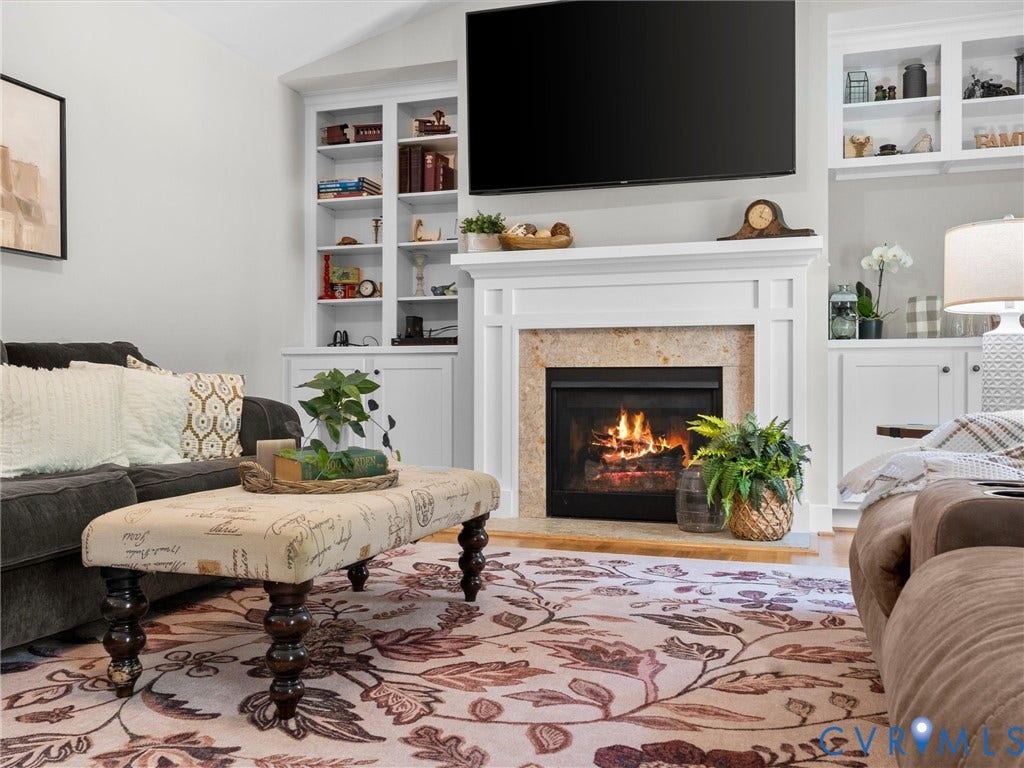 Living area featuring a gascfireplace with a stone surround and white mantel, flanked by built-in white cabinetry and shelving