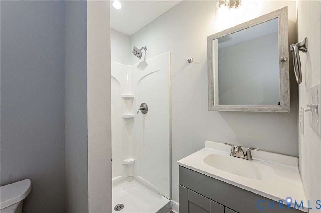 2015 Fordson Road, Richmond, VA 23229 Bathroom featuring a shower stall with built-in shelving, a vanity with a white countertop and gray cabinetry, a framed mirror, and brushed nickel fixtures