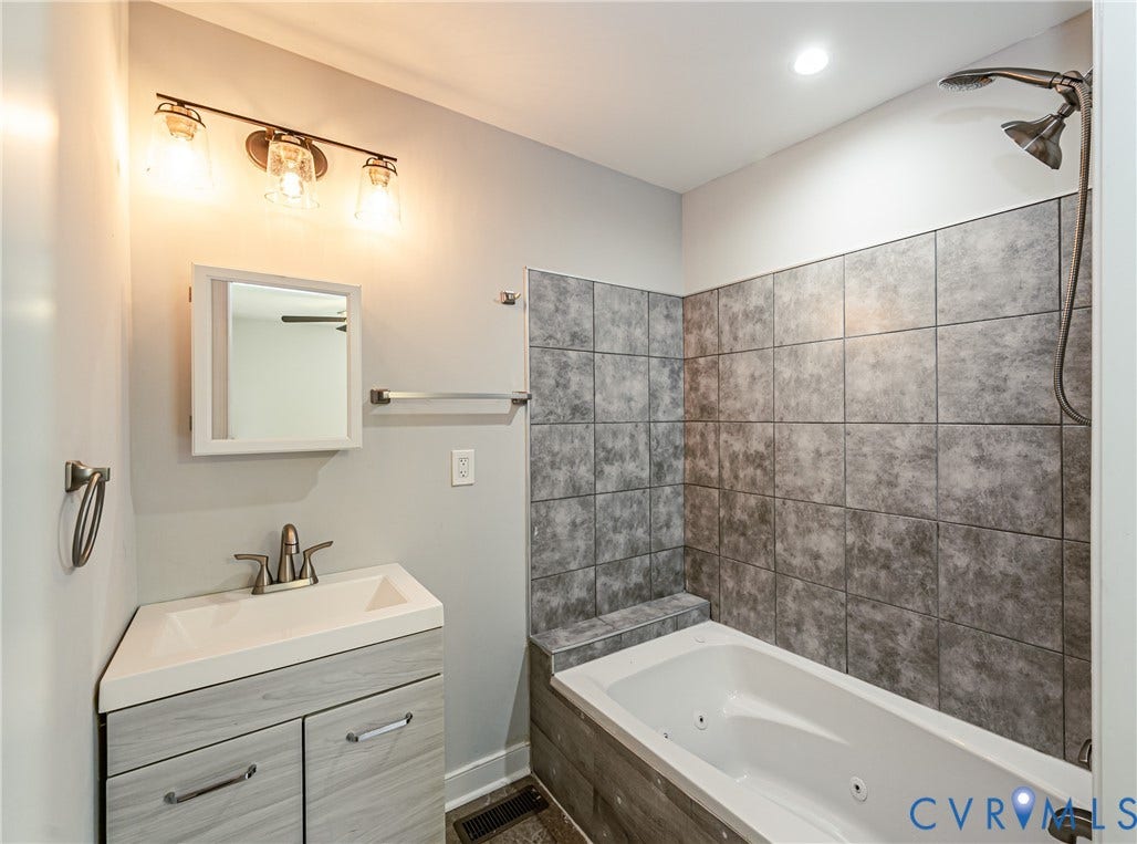 2015 Fordson Road, Richmond, VA 23229 Bathroom featuring a white jetted tub with dark gray tile surround and an integrated corner vanity