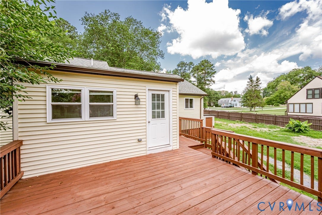 2015 Fordson Road, Richmond, VA 23229 Expansive wooden deck with coordinating railings, featuring a white exterior door with glass panes and two windows on the cream-colored siding