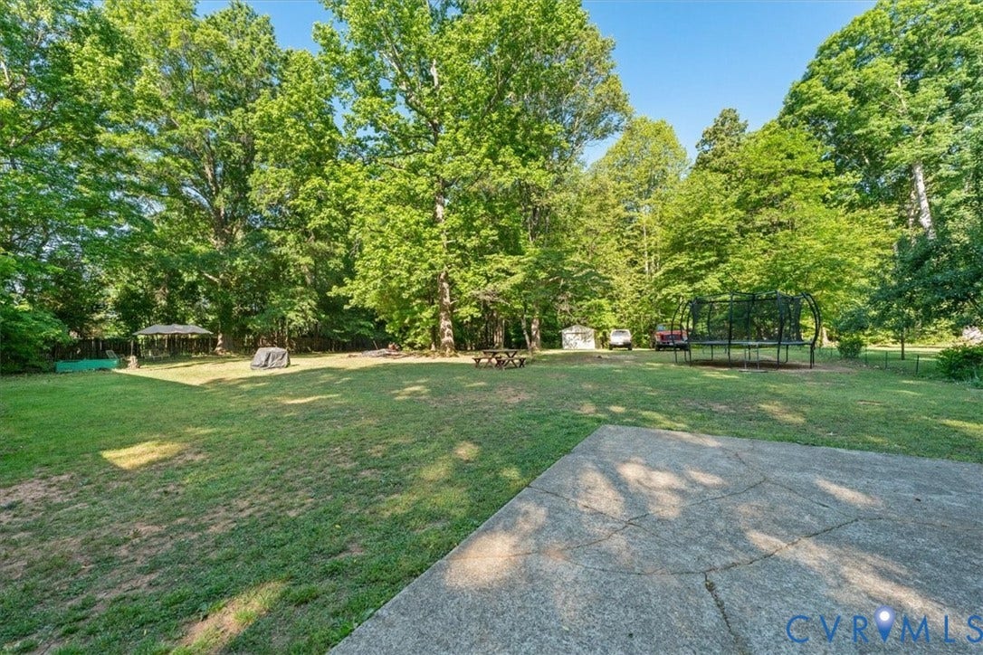 Expansive backyard featuring a concrete patio, a gazebo, mature trees, and a substantial grassy area