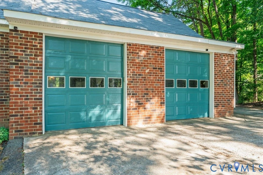 Two teal garage doors featuring upper window panels, set into a brick facade, with a concrete driveway approach