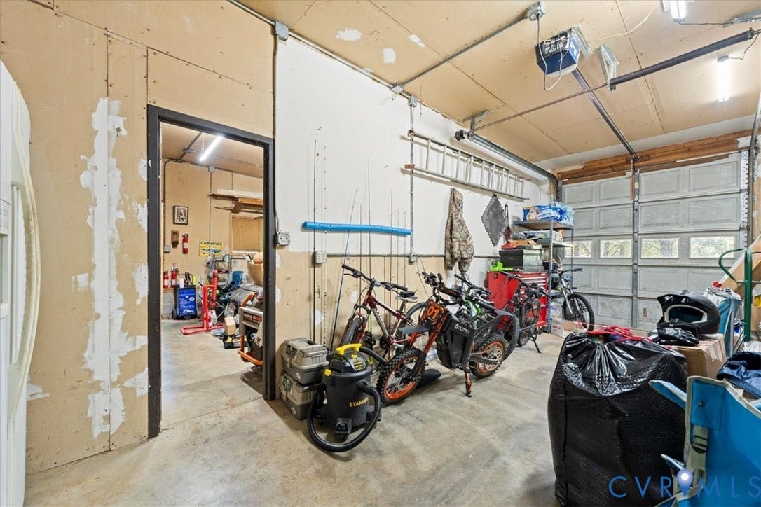 Utility garage space featuring a roll-up garage door with window panels, exposed ceiling joists, concrete flooring, and a standard interior door frame