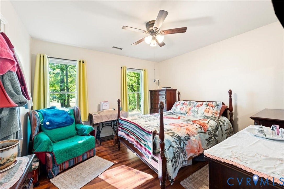 Room featuring wood-finish flooring, a ceiling fan with integrated lighting, and two windows providing natural light