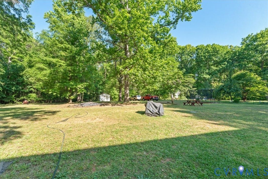 Expansive grassy yard area with mature trees and a white storage shed
