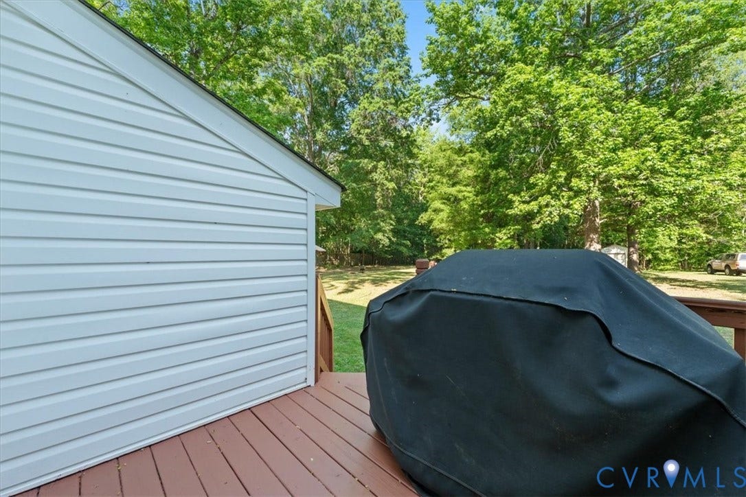 Rear exterior deck with light-colored siding and a wooded backdrop