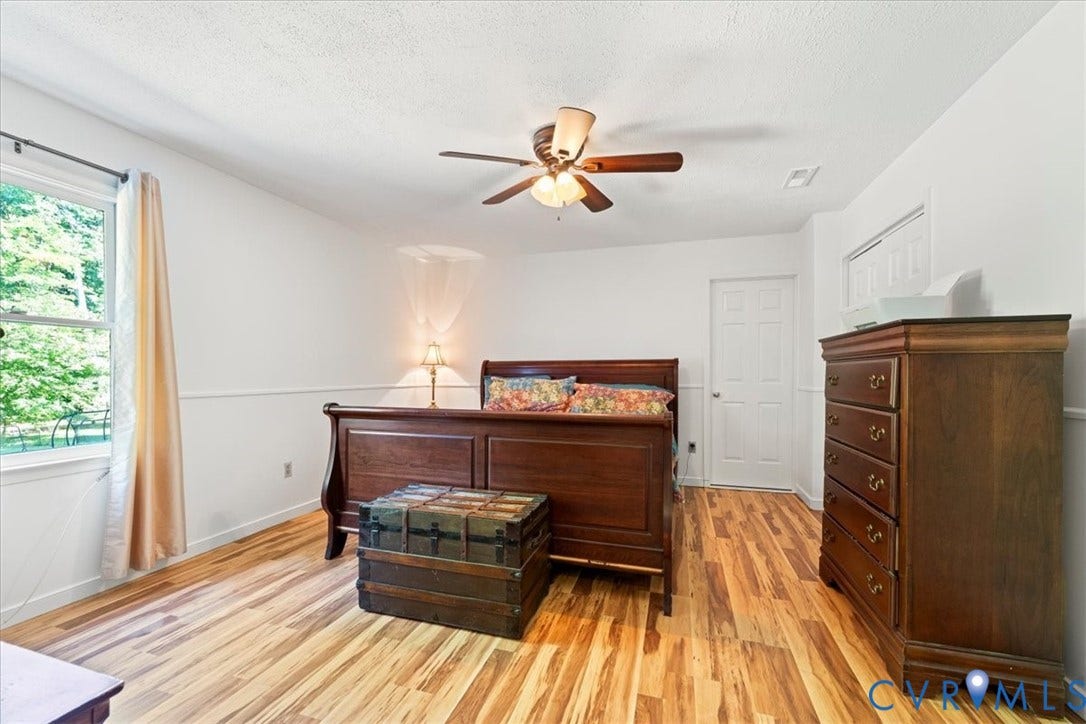 Spacious room featuring wood-finish flooring, white walls with wainscoting detail, a ceiling fan with integrated lighting, and a window providing natural illumination