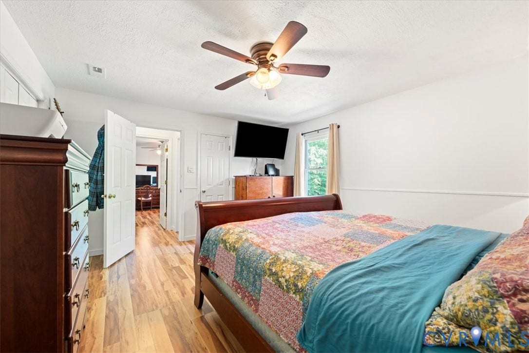 Bedroom featuring wood-finish flooring, a ceiling fan with integrated lighting, white walls, and a window with natural light