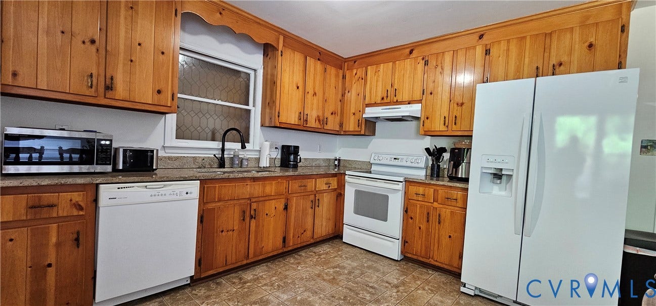 Kitchen featuring abundant wood cabinetry, stone-finish countertops, white appliances, a contemporary black faucet, and patterned flooring
