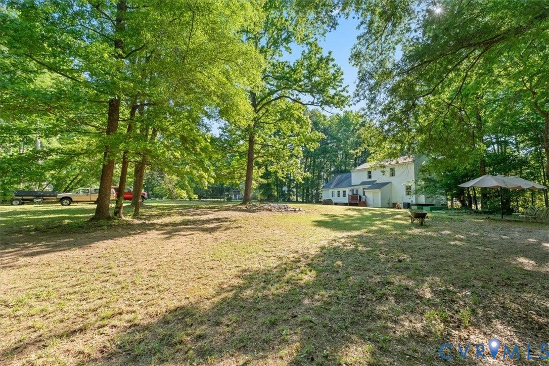 Expansive rear yard featuring mature trees and a two-story residence with a light-colored siding