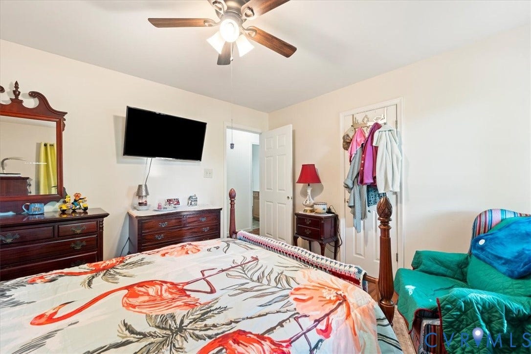 Light-toned bedroom featuring a ceiling fan with integrated lighting, a wall-mounted television, and a white paneled door