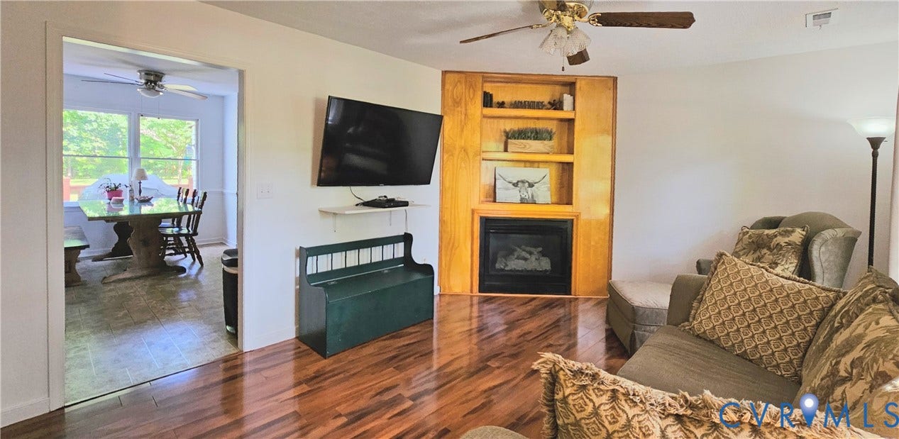 Living area featuring wood-finish flooring, a built-in fireplace with a hearth, integrated shelving, and a ceiling fan