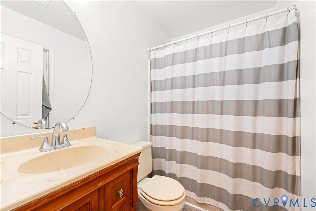 Bathroom featuring a wood-finish vanity with an integrated sink and light-colored countertop, a chrome two-handle faucet, and a round wall-mounted mirror