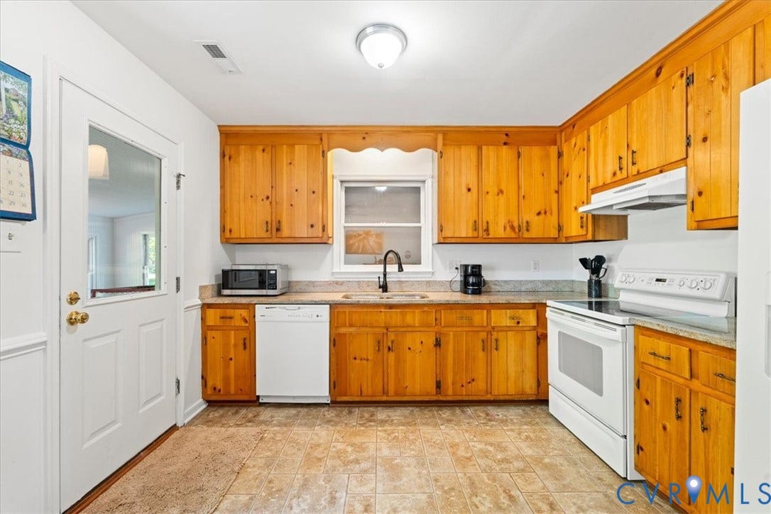 Kitchen featuring wood cabinetry, light-toned countertops, tile flooring, and white appliances