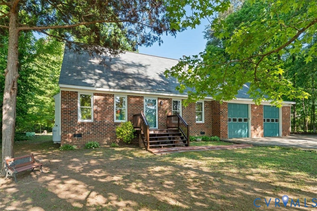 Brick exterior residence featuring a gray shingle roof, multiple windows, a rear wooden deck with stairs, and two teal garage doors