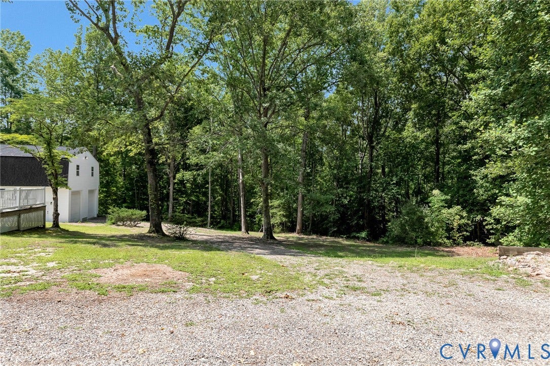348 Forest Lane, Timberland Estates, King William, VA 23086 Expansive gravel parking area bordered by mature trees and a white two-story structure with two garage doors