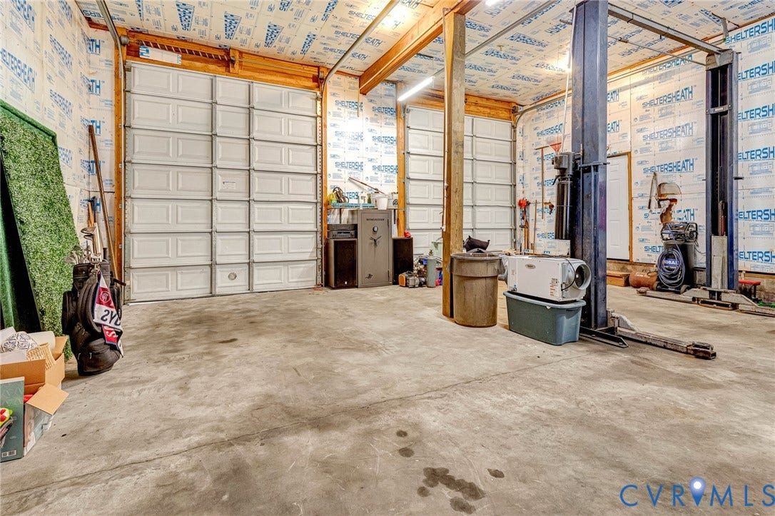 348 Forest Lane, Timberland Estates, King William, VA 23086 Utility space featuring two overhead doors, exposed wood beams, concrete flooring, and an integrated vehicle lift system