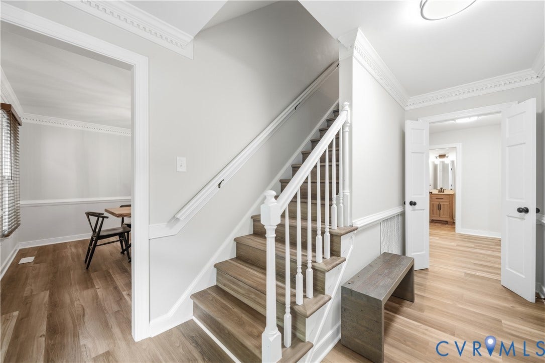 Entryway featuring a wood-finish staircase with white balusters, wainscoting, crown molding, and light wood-finish flooring