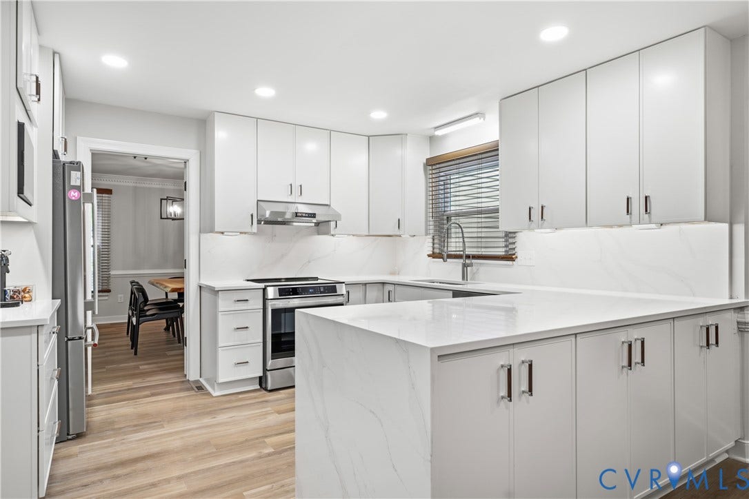 Modern kitchen featuring white flat-panel cabinetry, light-toned wood-finish flooring, and white countertops with integrated backsplash