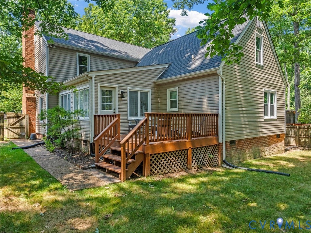 Exterior rear elevation featuring a wood deck with lattice skirting, a sunroom extension, and a red brick chimney