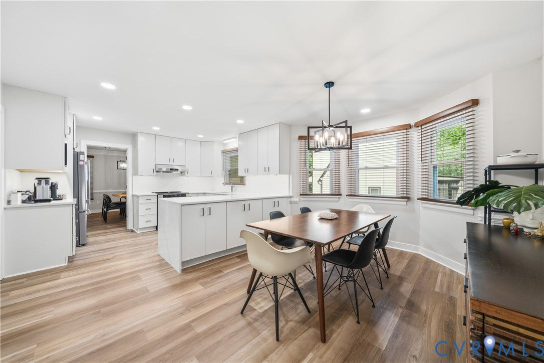 Open-concept kitchen and dining area featuring light wood-finish flooring, white cabinetry, a central kitchen island with countertop seating, and recessed lighting