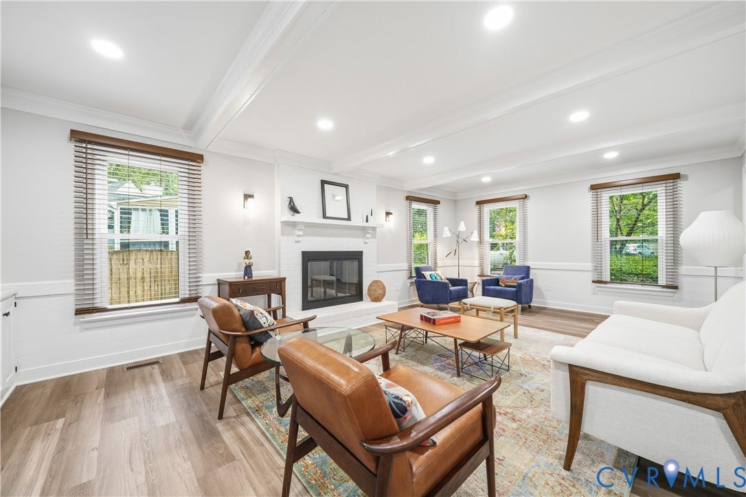 Spacious living area featuring wood-finish flooring, white wainscoting, recessed lighting, and a white fireplace with a dark hearth