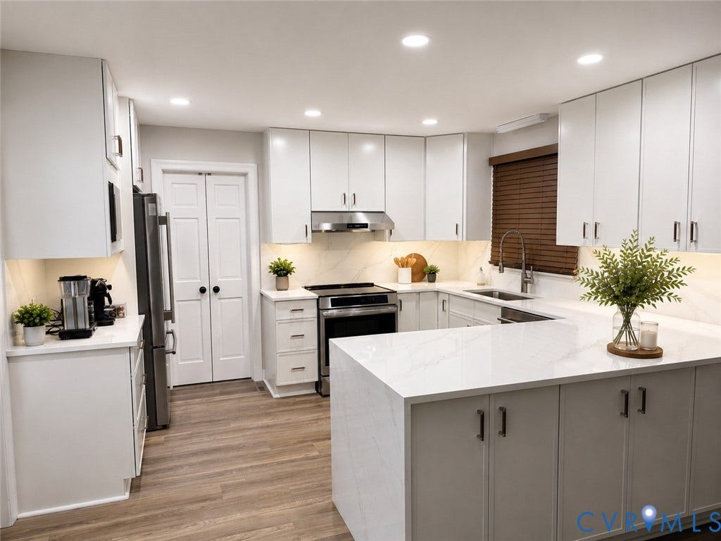 Contemporary kitchen featuring white cabinetry with dark hardware, a center island with waterfall-edge countertops, stainless steel appliances, and wood-finish flooring