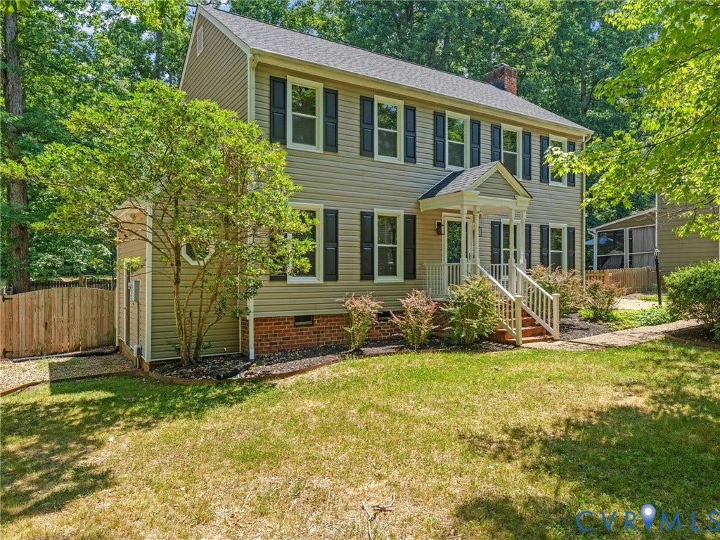 Traditional two-story residence featuring light-colored siding with dark window shutters, a covered front porch with white railings, and a brick foundation