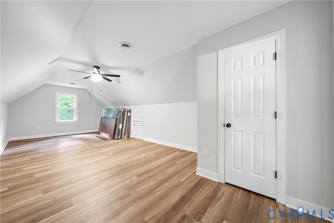 Spacious room featuring vaulted ceilings, wood-finish flooring, a ceiling fan with integrated lighting, and a paneled white door