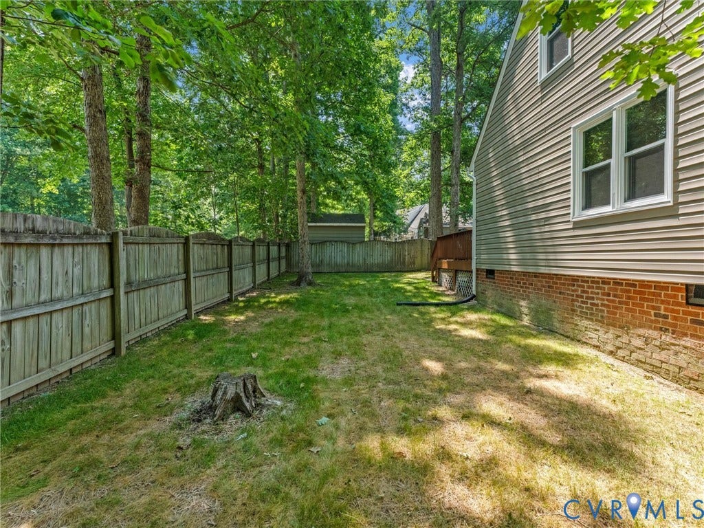 Expansive backyard featuring a wood privacy fence, mature trees, and a partial brick foundation