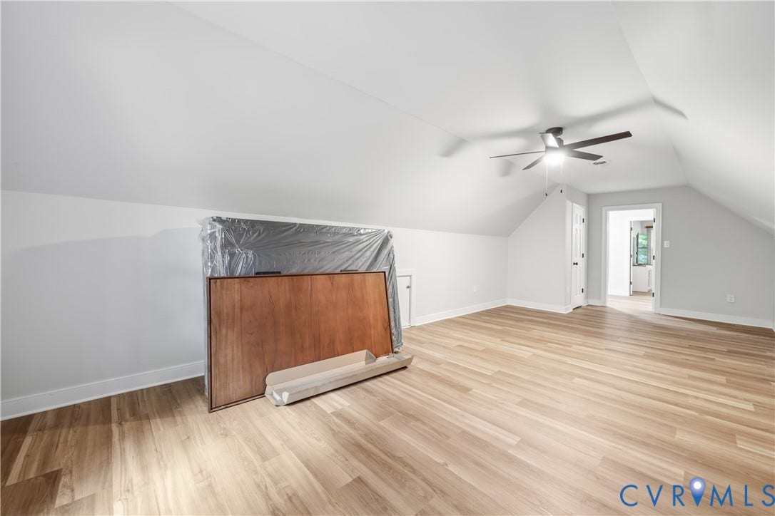 Spacious room featuring vaulted ceilings, wood-finish flooring, recessed wall space, and a ceiling fan with integrated lighting