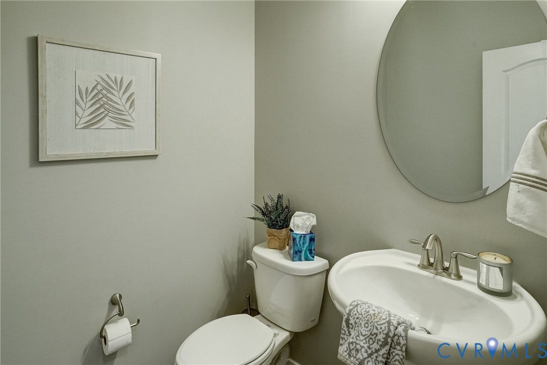 18024 Twin Falls Lane, Aston Oaks, Moseley, VA 23120 Pedestal sink with brushed nickel faucet, round frameless mirror, and a white toilet