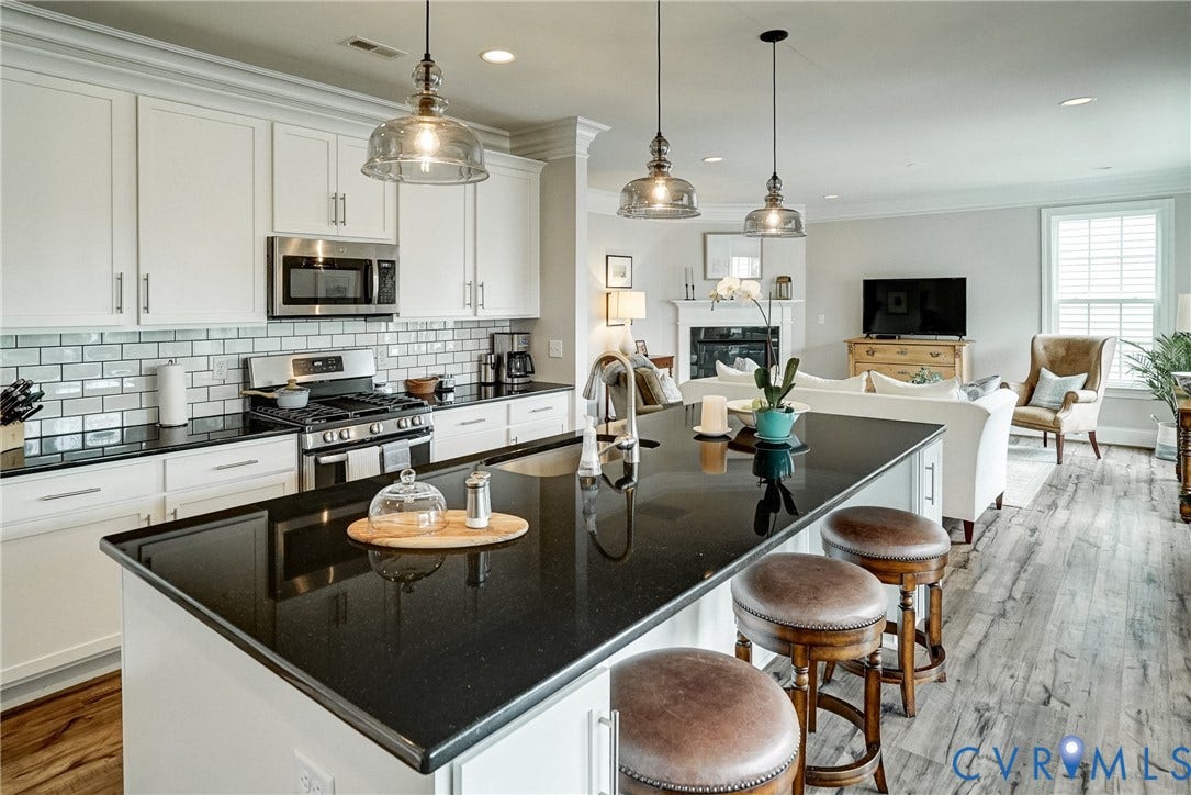 18024 Twin Falls Lane, Aston Oaks, Moseley, VA 23120 Open-concept kitchen featuring an expansive black countertop island with pendant lighting, white cabinetry, stainless steel appliances, and a subway tile backsplash