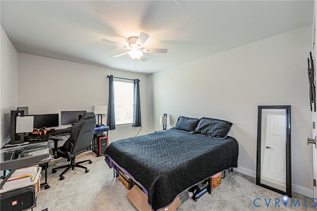 7627 E Danube Loop, New Kent, VA 23124 Spacious room featuring light gray carpet, a ceiling fan with integrated lighting, and a large window with privacy blinds