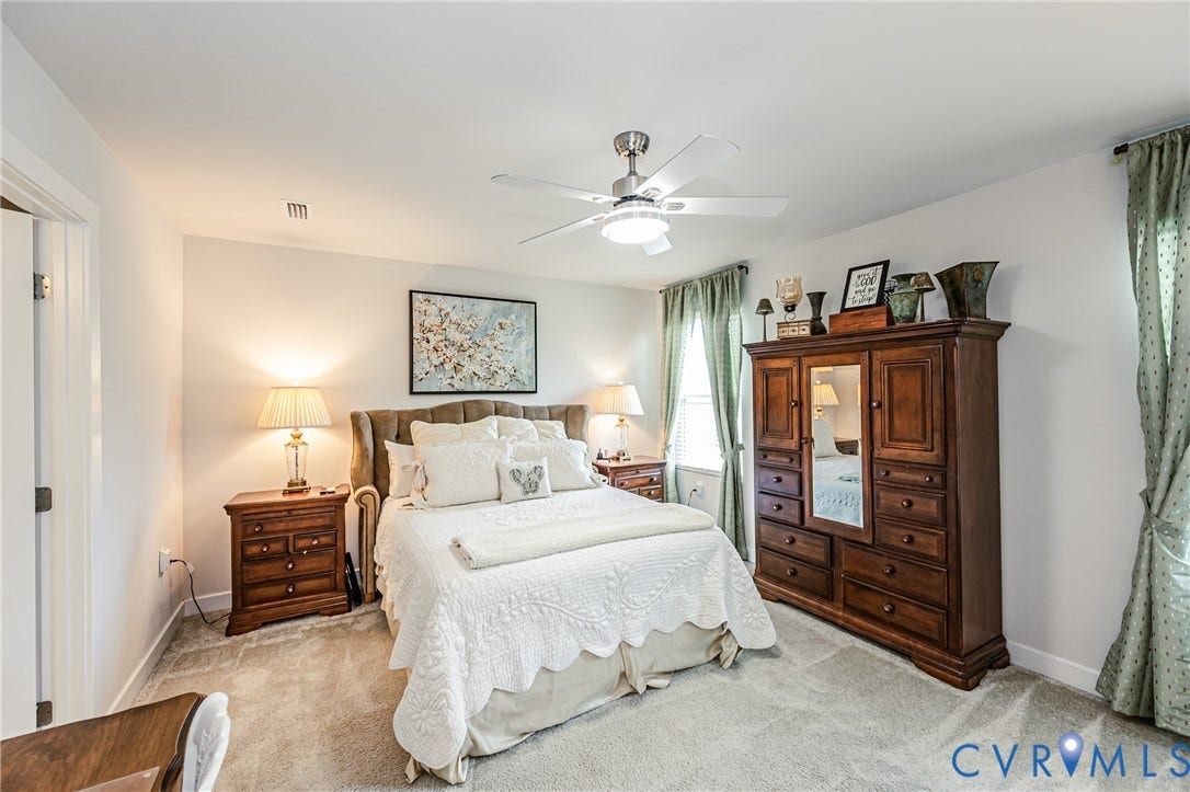 7627 E Danube Loop, New Kent, VA 23124 Carpeted bedroom with a ceiling fan, two windows featuring drapes, and a white door frame