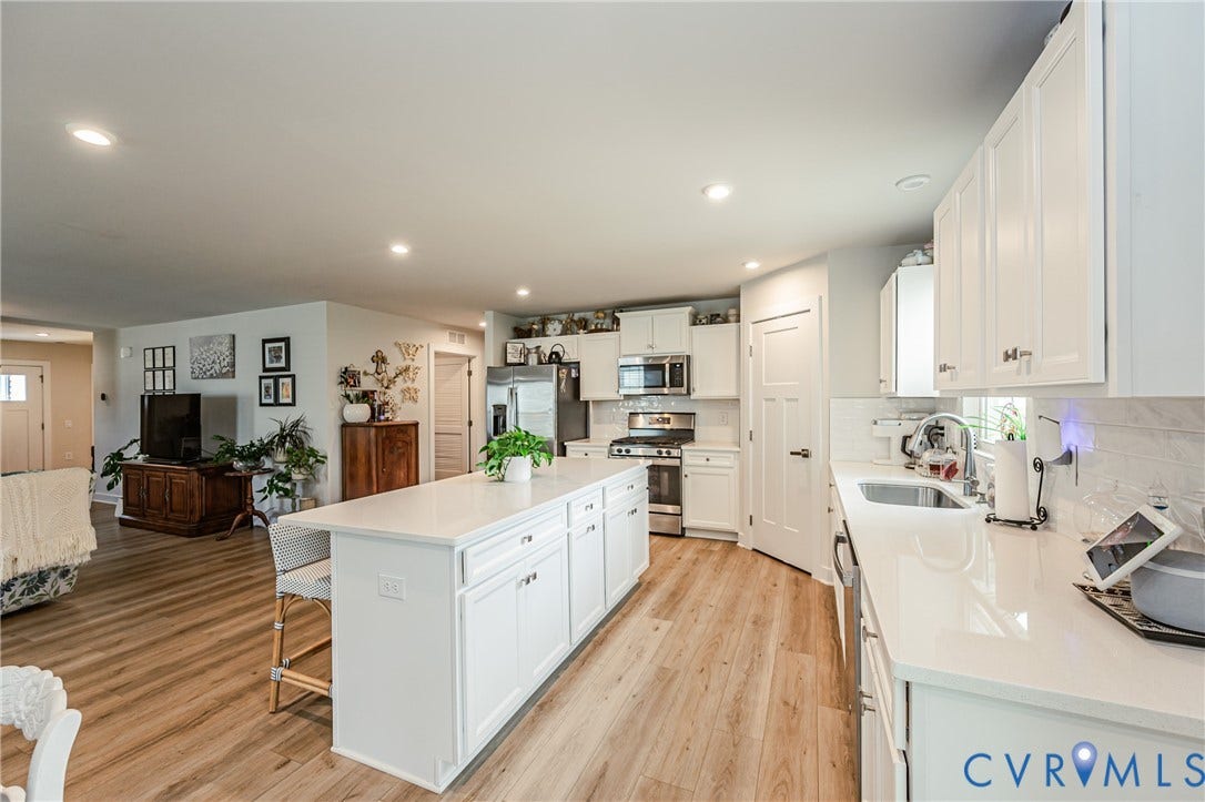 7627 E Danube Loop, New Kent, VA 23124 Open-concept kitchen featuring an expansive island with seating, white shaker-style cabinetry, quartz countertops, and stainless steel appliances