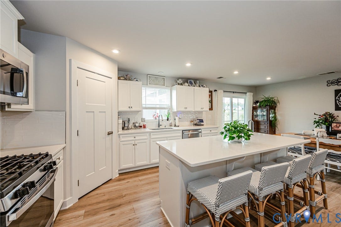 7627 E Danube Loop, New Kent, VA 23124 Bright kitchen featuring a substantial island with countertop seating, white cabinetry, stainless steel appliances, wood-finish flooring, and recessed lighting