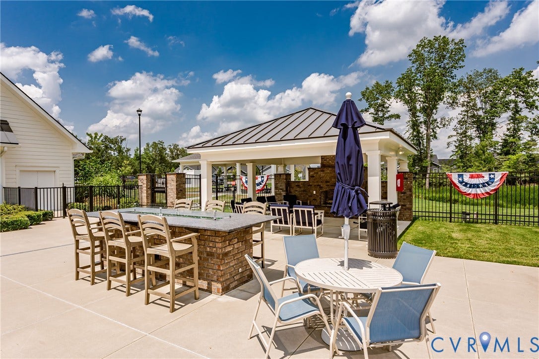 7627 E Danube Loop, New Kent, VA 23124 Expansive outdoor patio featuring a brick-clad bar with seating, a covered pavilion with a metal roof, and a perimeter fence